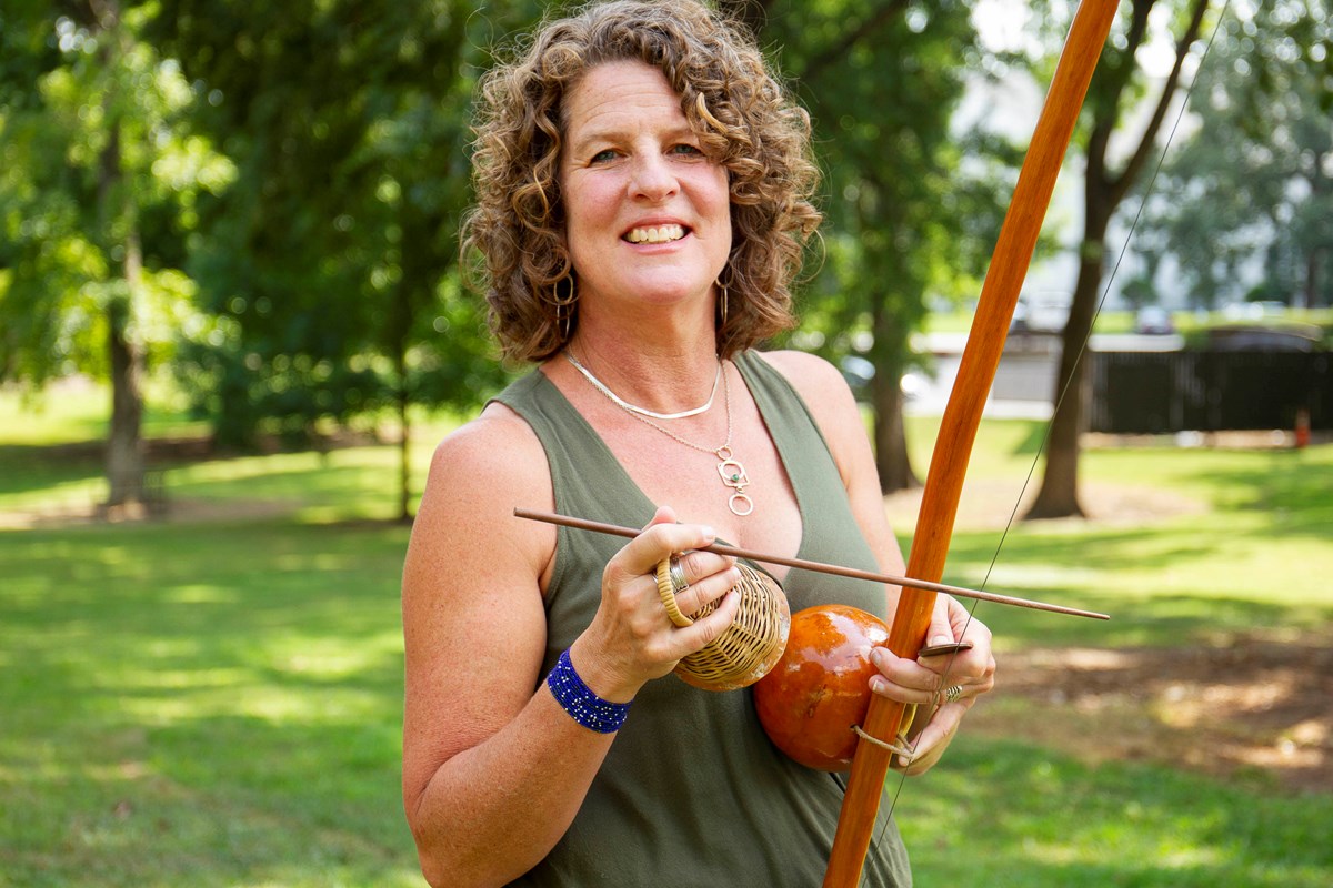 Katya Wesolowski holding a Berimbau instruments outdoors.