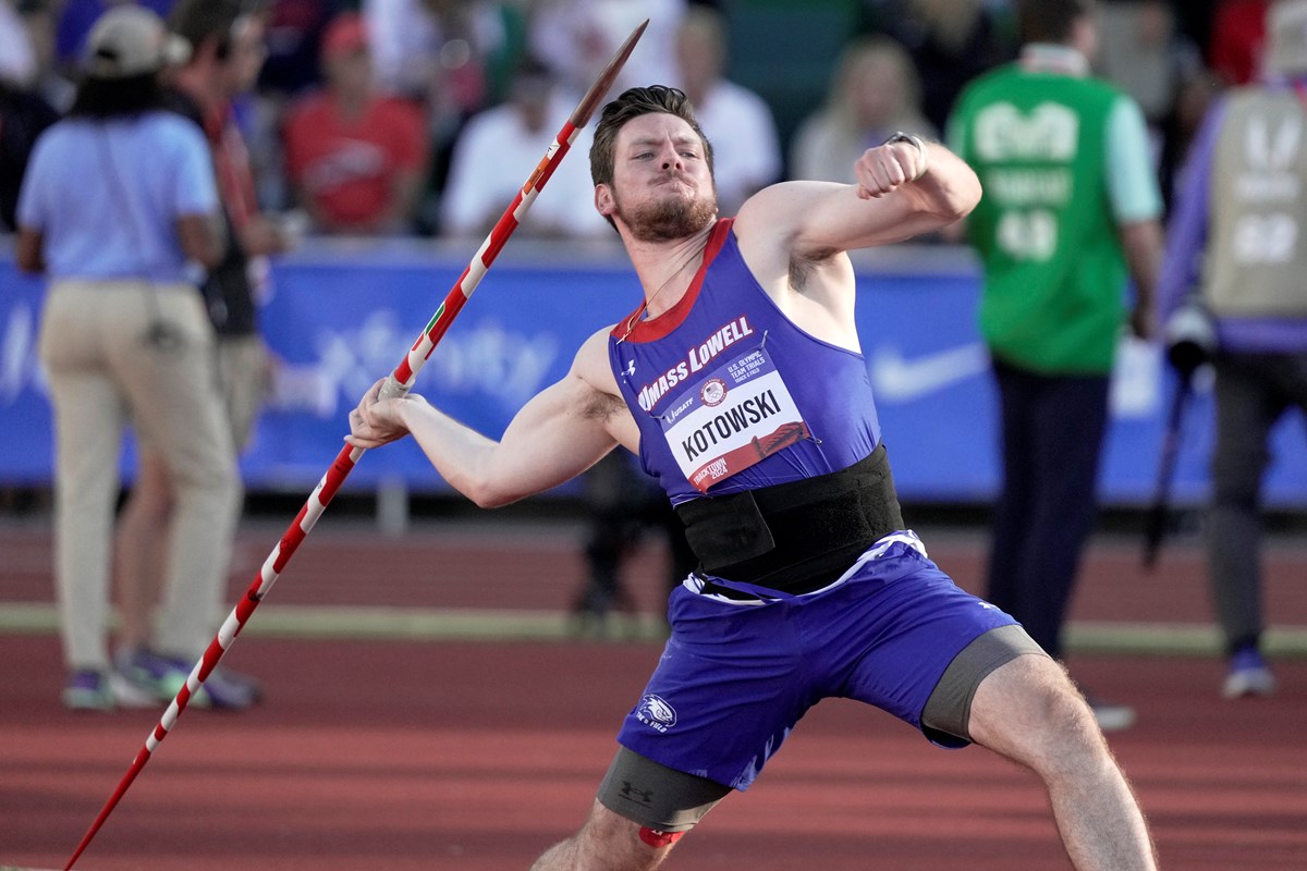 A person in a blue track uniform throws a javelin in a competition.