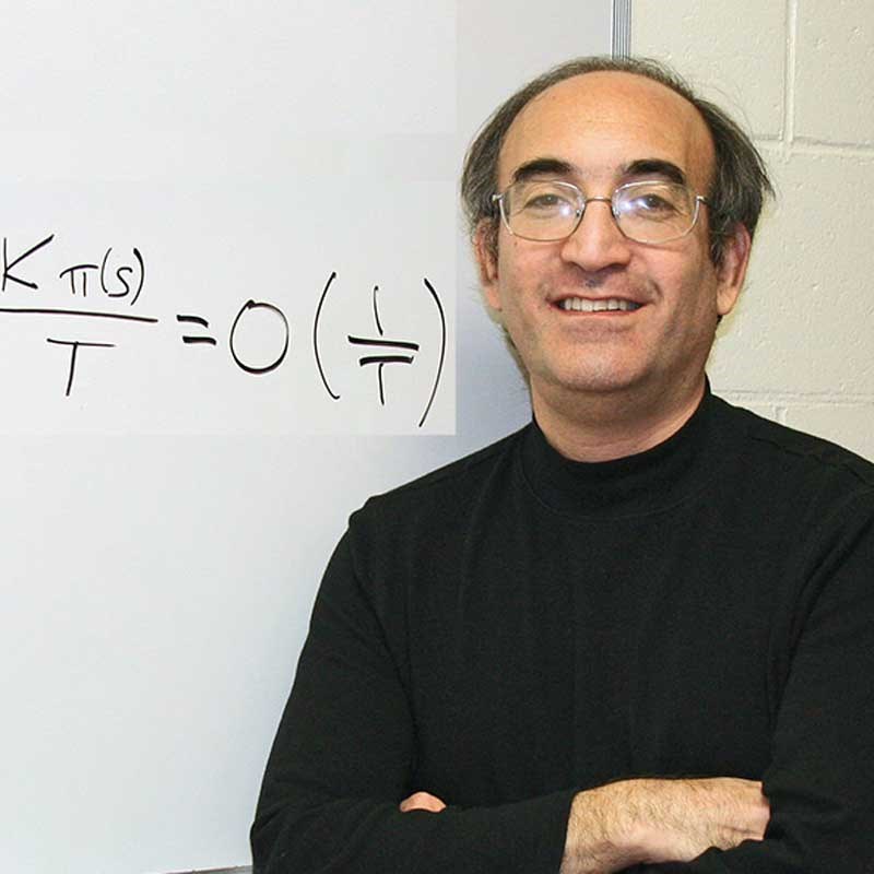 UMass Lowell math faculty James Propp smiling next to whiteboard