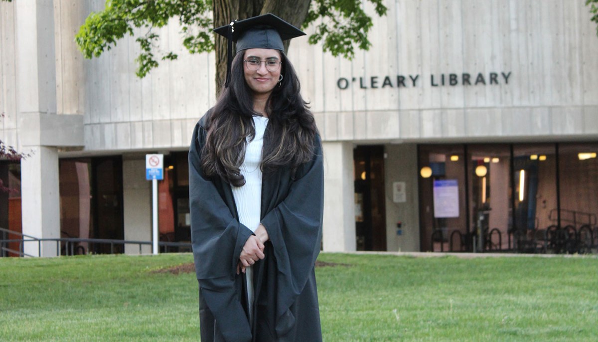 Namrata Chauhan poses for photo in her graduation gown in front of O'Leary Library.