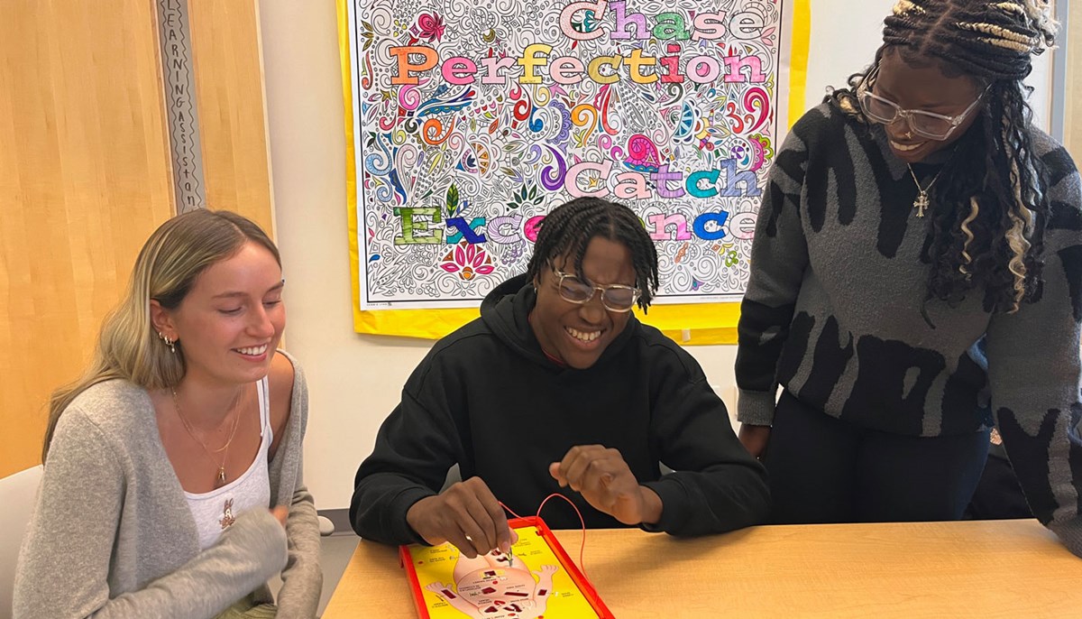 Nosagiegbon (Sai) Igiede sits between two students while playing a game.