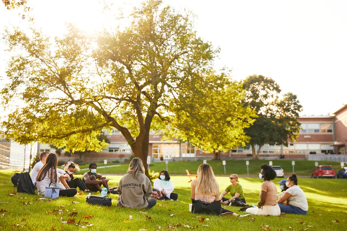 Several students sit in a circle on the grass in the middle of UMass Lowell's South Campus.