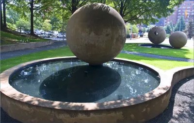 Giant round stone hovering over pool of water with other round stones in background