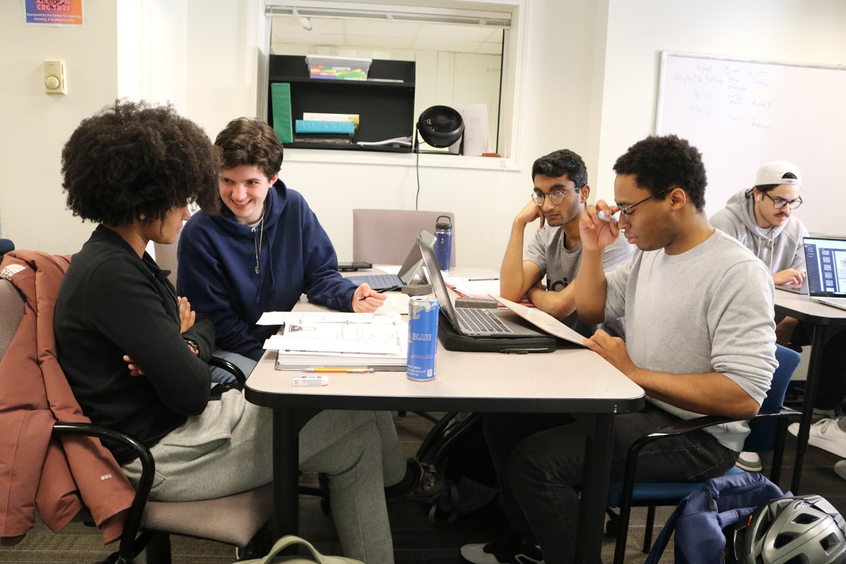 Three students and a tutor sit and discuss class work at the UMass Lowell tutoring center.