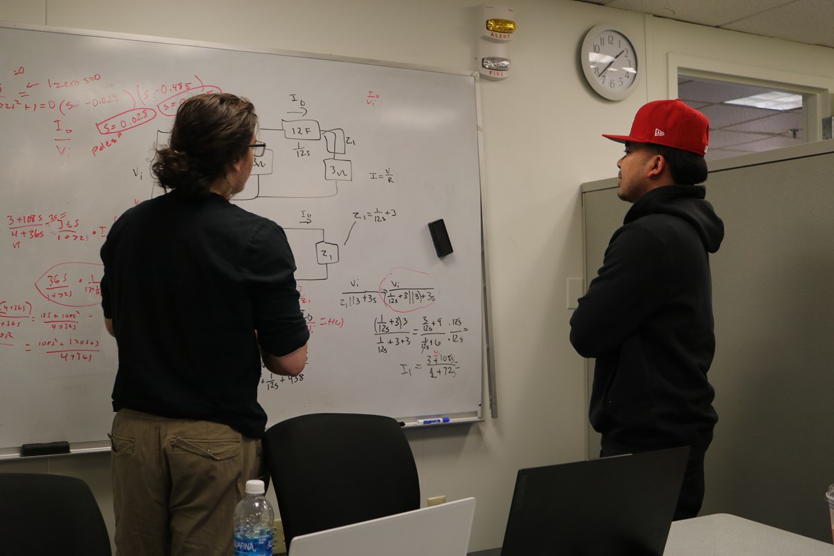 A student and a tutor discuss mathematical equations on a white board.