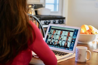 Stock Image: Woman sitting at desk with laptop computer in front of her with video conference showing 9 people on screen.