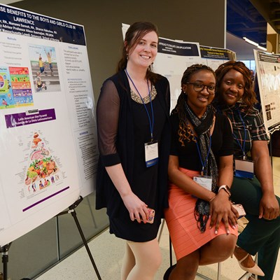 Three students stand and sit in front of their posters.