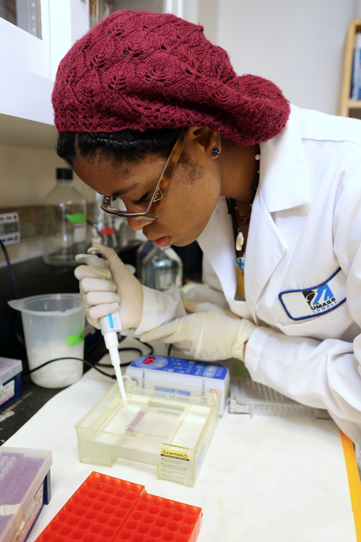 A student in a lab leans over a table with a pipette putting something into another container.