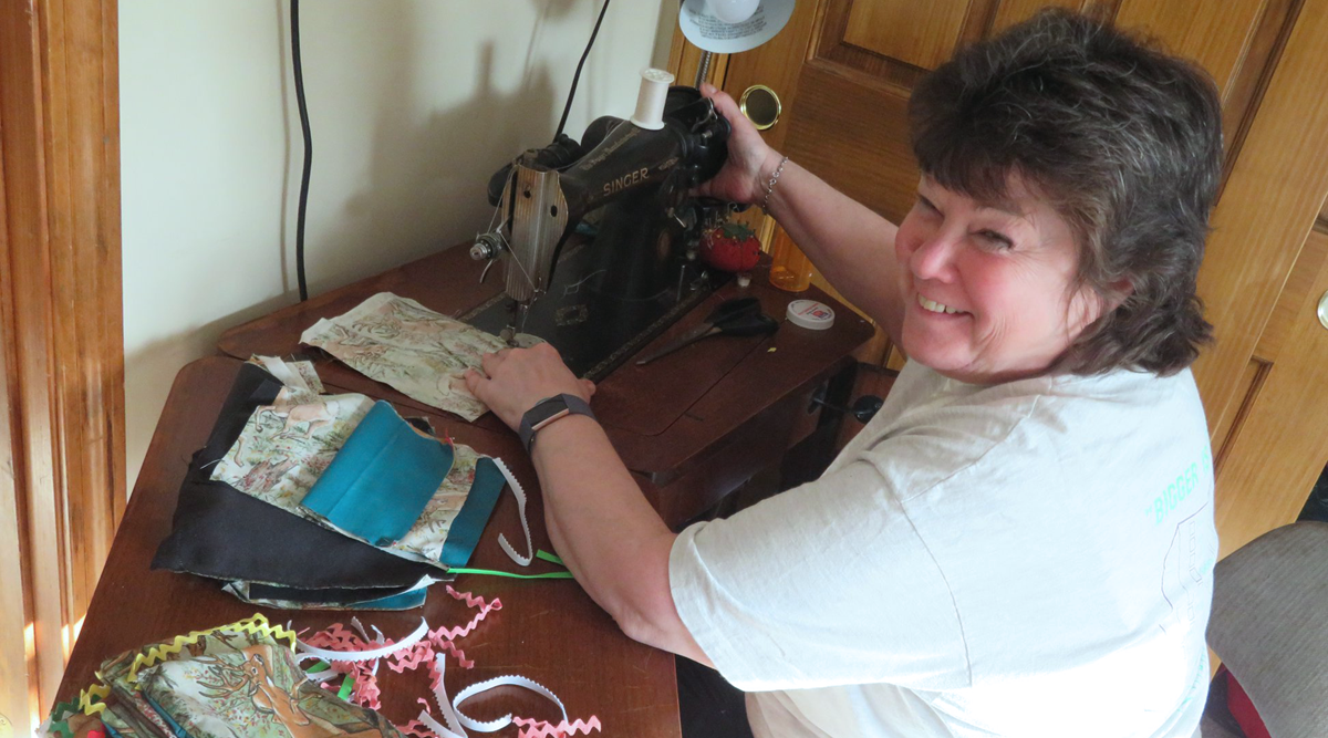 Lisa Gagnon sitting down at her vintage Singer sewing machine with colorful, sewn face masks.