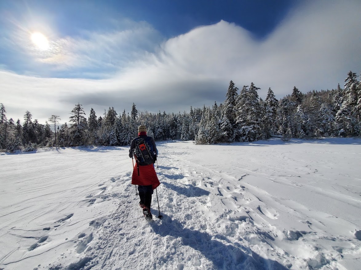 Person hikes across a frozen lake backlit by sun.