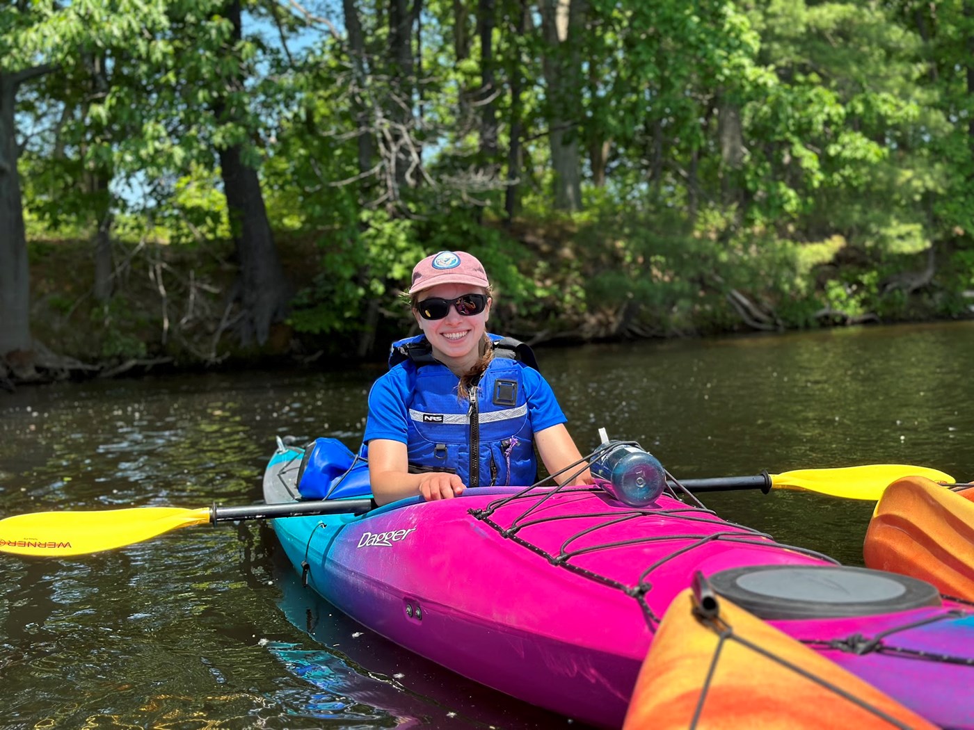 A person wearing sunglasses and a hat floats in a kayak on a bright sunny day.