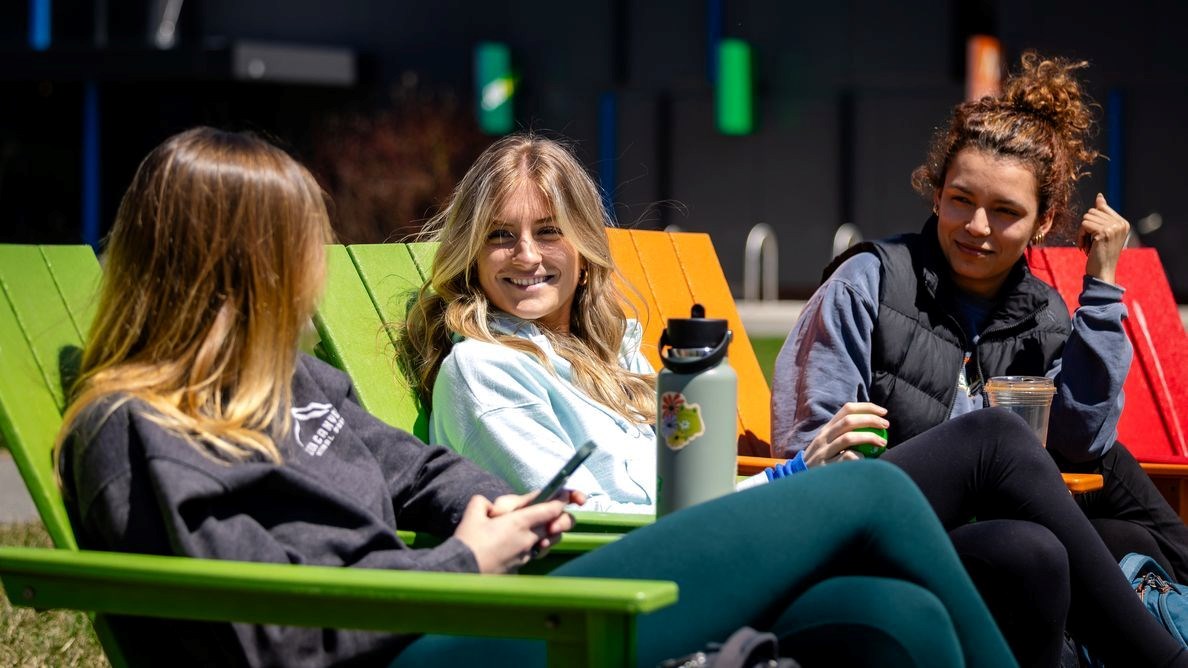 Three students seated on colorful Adirondack chairs