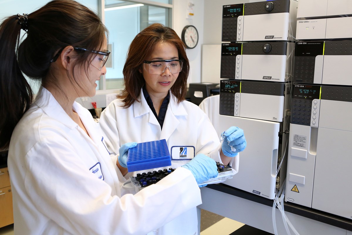 Two female laboratory personnels in lab coats and safety goggles working with a tray of tubes.