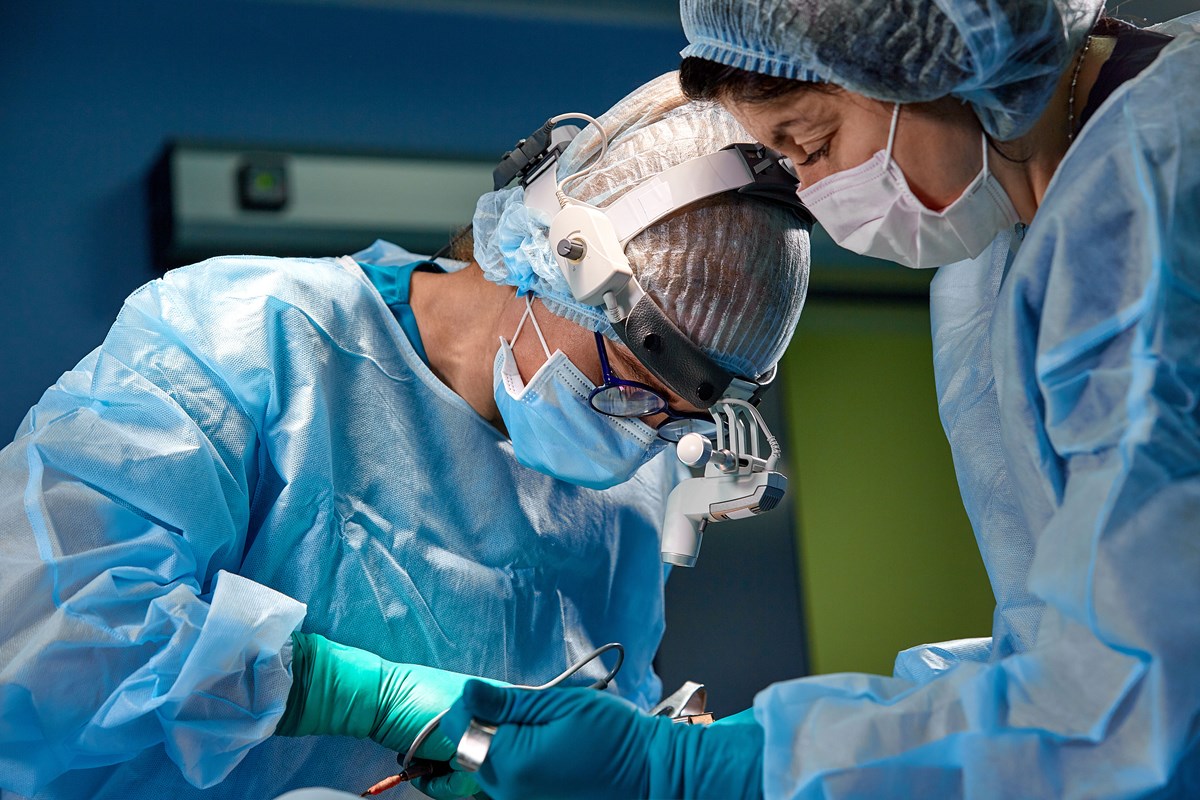 Two surgeons in blue gowns and masks performing a medical procedure in an operating room.