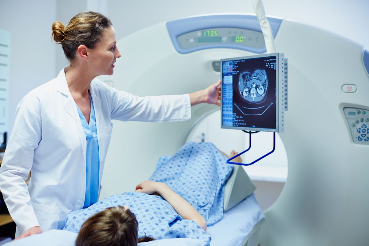 Doctor displaying a CT scan on a monitor while a patient lies inside the scanner.