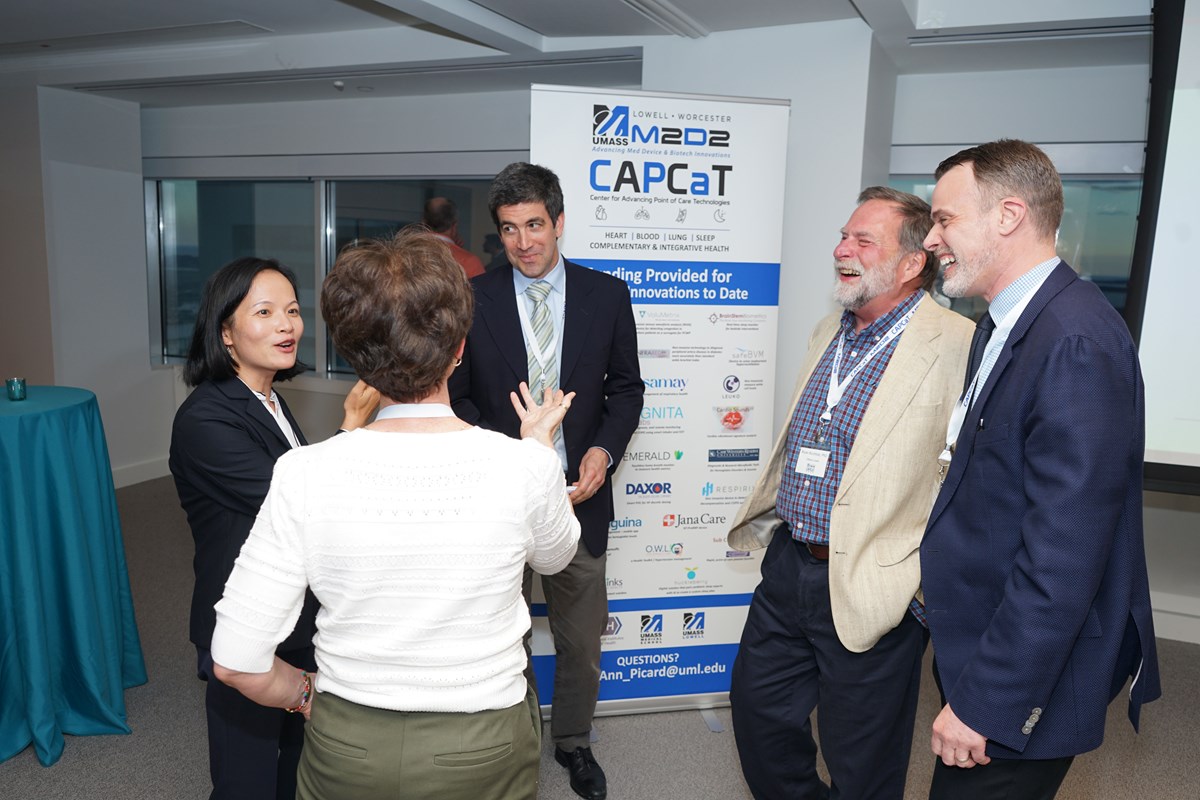 A group of five attendees talking in front of a banner at the M2D2 CAPCaT conference.