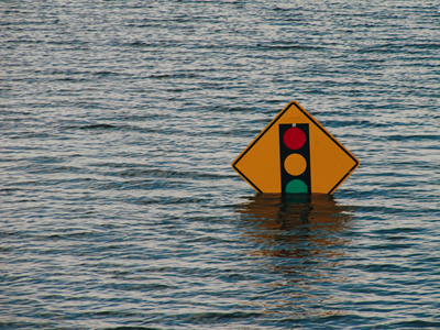 Yellow street sign showing traffic light just above flood waters.