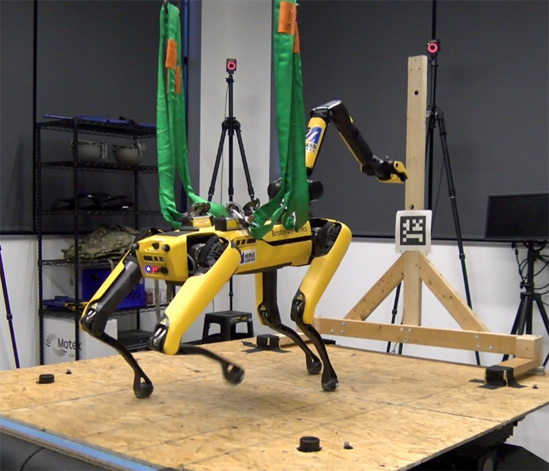 Boston Dynamics Spot robot with arm walking on a tilted platform.